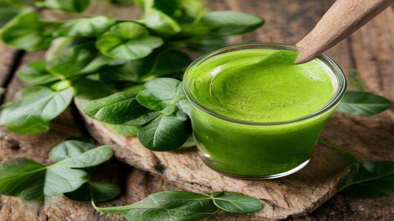 Moringa powder in a wooden spoon alongside fresh moringa leaves on a South African kitchen counter